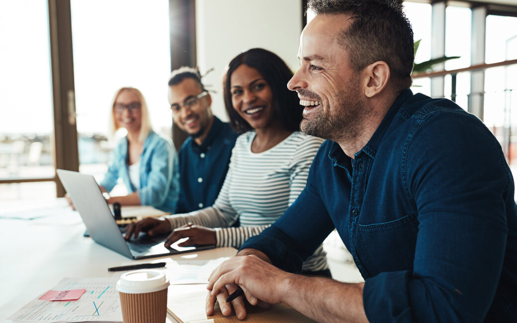Mature businessman laughing while sitting with a diverse group of coworkers during a meeting in an office