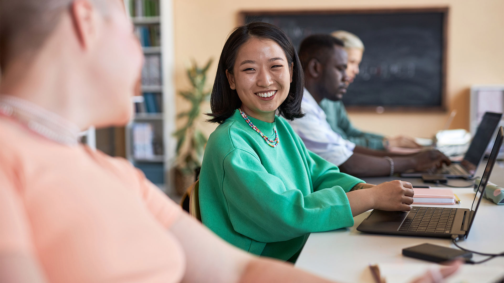 Young cheerful Asian woman looking at her classmate or coworker
